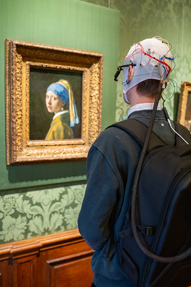 Mauritshuis - Un soggetto dello studio neurologico di fronte al dipinto La ragazza con l'orecchino di perla con indosso una cuffia EEG e un eye tracker